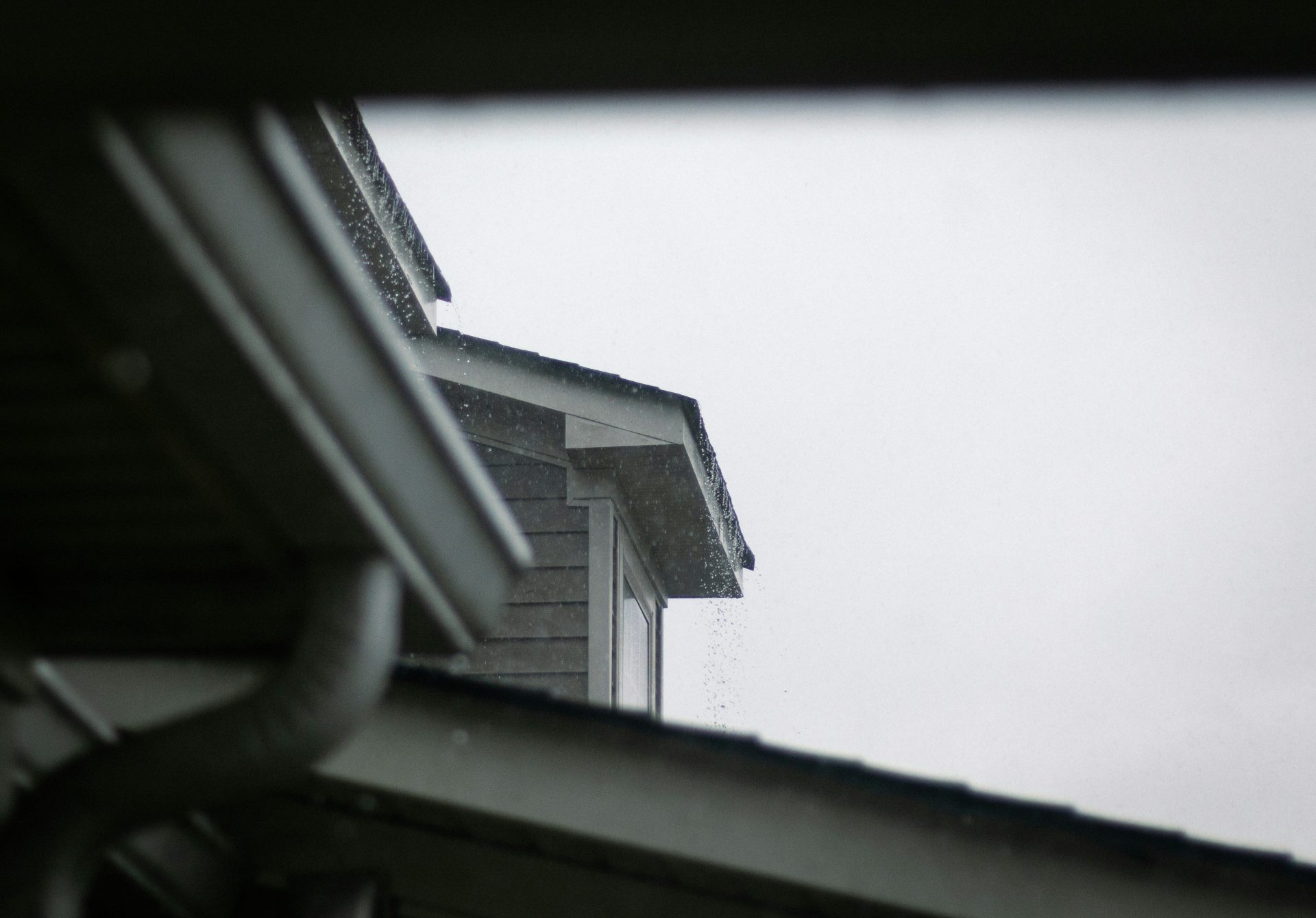 A house roof and gutter system against a grey sky.