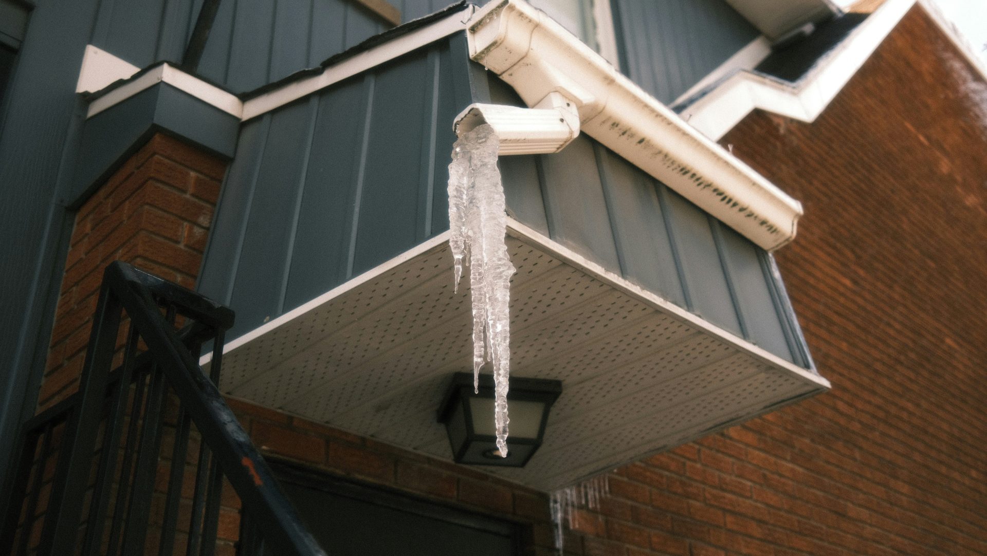 Long icicles hang from a white gutter on a building.
